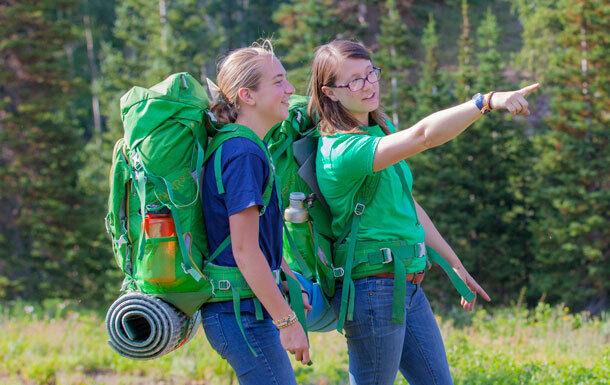 Two campers with large backpacks hiking and looking out at the forest